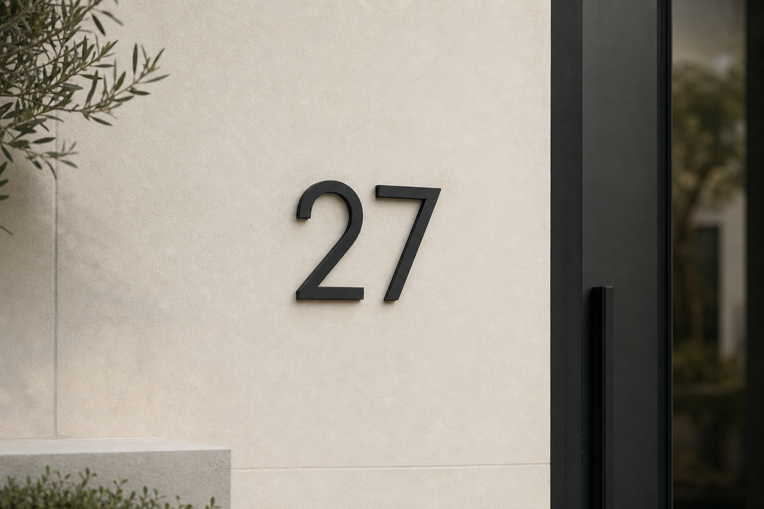 Standaard huisnummer 27 op een lichte pleistergevel, olijfboom aan de zijkant